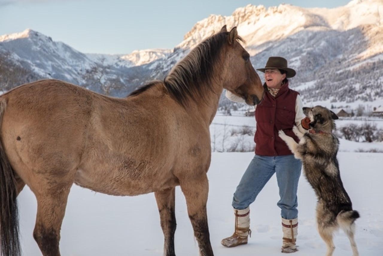 Julie Anderson visits with an old mustang on the Anderson Ranch in Tom Miner Basin, and her dog, Sage, who was rescued from Alaska.  "As women, there's another level of maternal connection that occurs—that is where we shine and find safety within ourselves," says Julie in reference to horses. Photo by Louise Johns