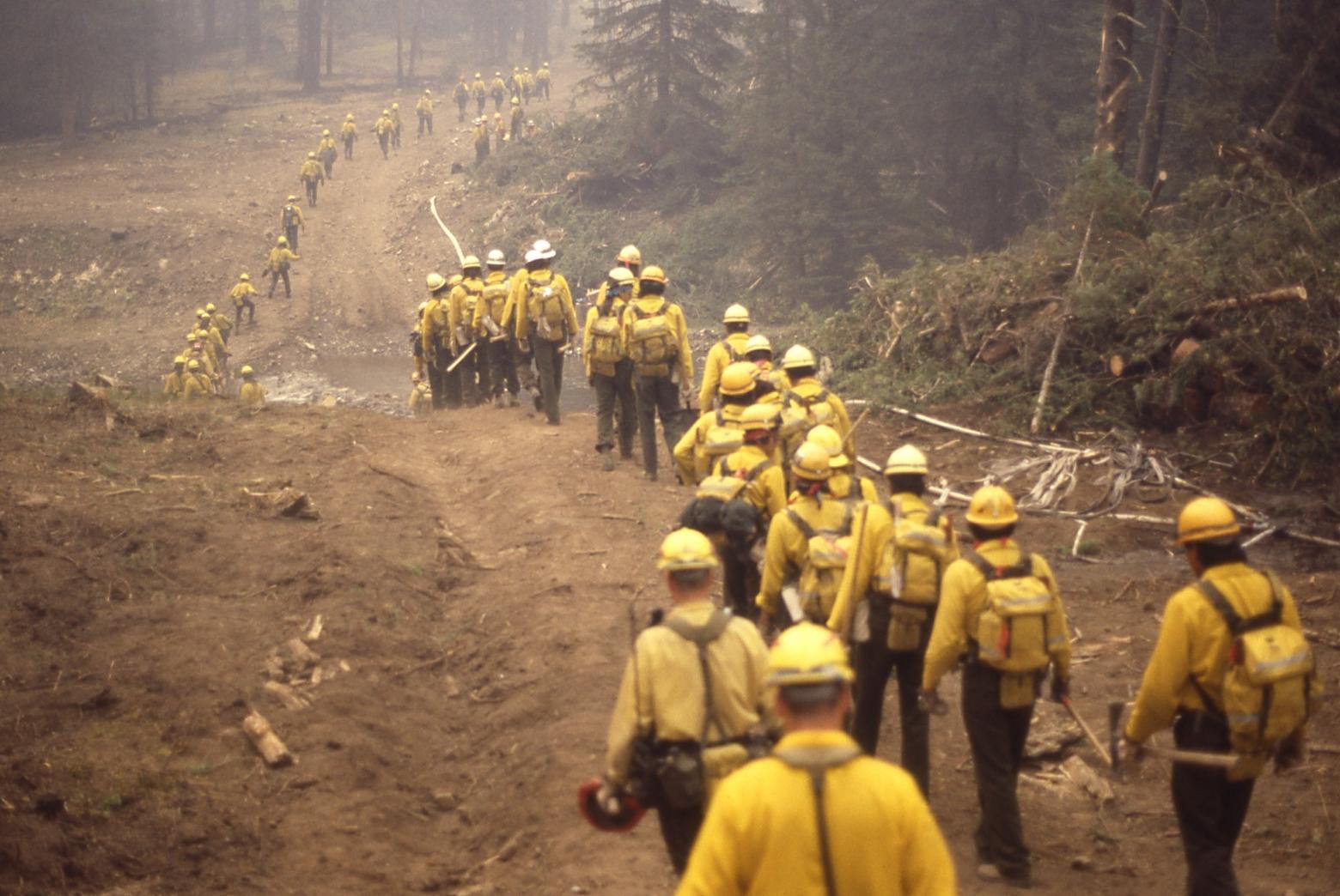 On Nov. 17, federal wildland firefighters face a pay cliff, which could cause massive workforce losses of up to 50 percent, according to the U.S. Forest Service. Here, military firefighters walk to buses near the Northeast Entrance of Yellowstone National Park during the fires of '88. Sept. 4, 1988. Photo by Jim Peaco/NPS