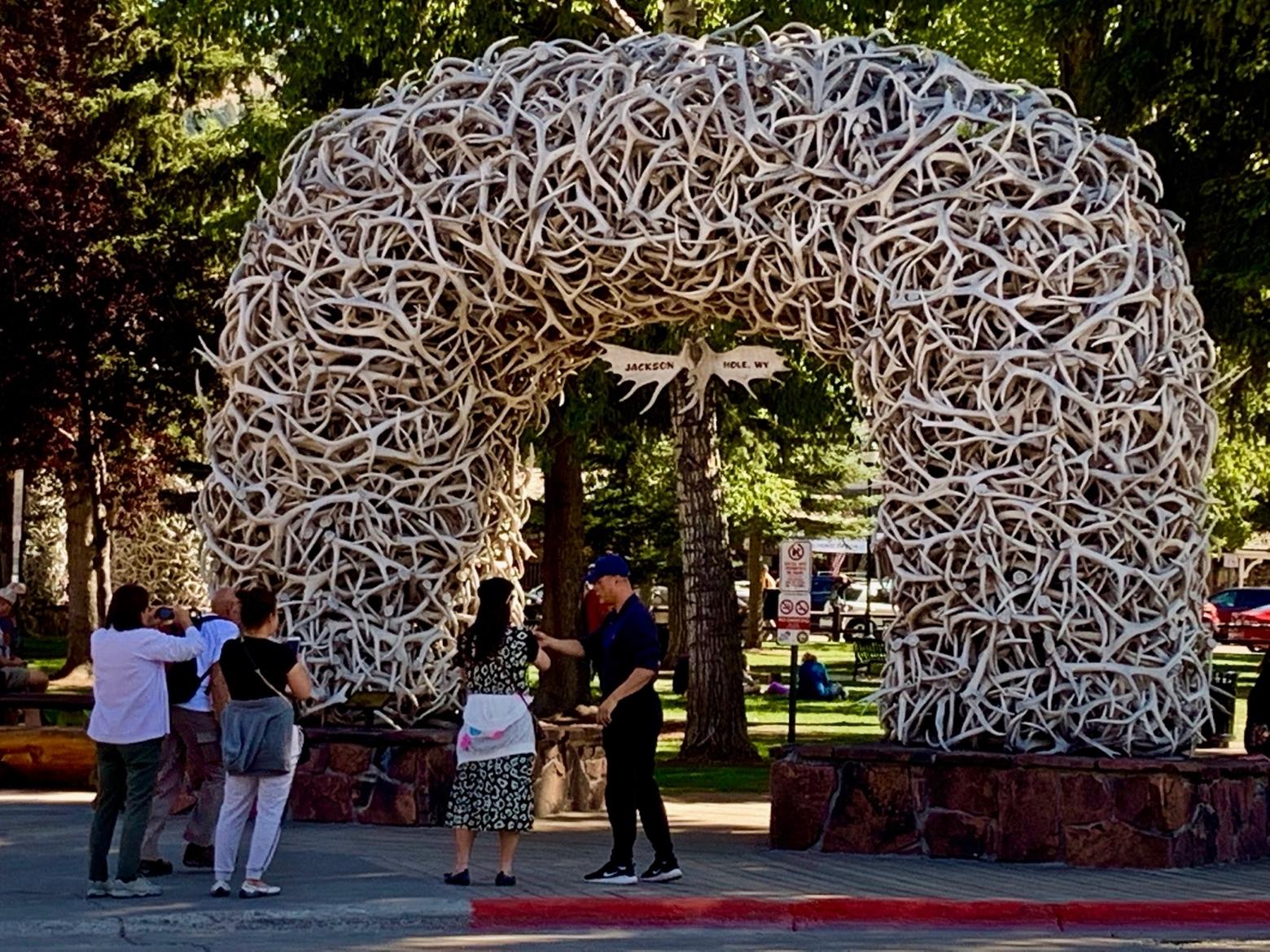 Tourists pose in front of a famous archway made of elk antlers that adorns the entrance to the downtown square in the center of Jackson, Wyoming.  How does a town sustain economic growth and still protect the natural environment, provide affordable places to live for local employees and still manage to maintain its character?  Photo by Todd Wilkinson