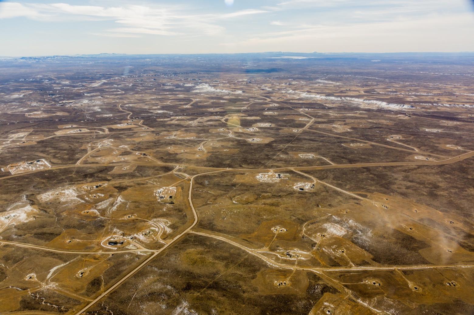 The Jonah Natural Gas Field in the Upper Green River Basin. Wyoming made a big gamble on fossil fuel energy development as a job creator and source of revenue for the state. But its "all of the above" approach promoting both gas development and coal production backfired when  market forces, driven by a glut of cheap gas, caused coal prices to spiral. Some coal-fired power plants retrofitted to burn gas and coal companies in Wyoming declared bankruptcy. In reality, Wyoming isn't reeling from "a war on coal" by environmentalists but being torpedoed by supply-side economics. The chances that the state's fortunes will recover don't look good any time soon. Photo courtesy Ecoflight (ecoflight.org)