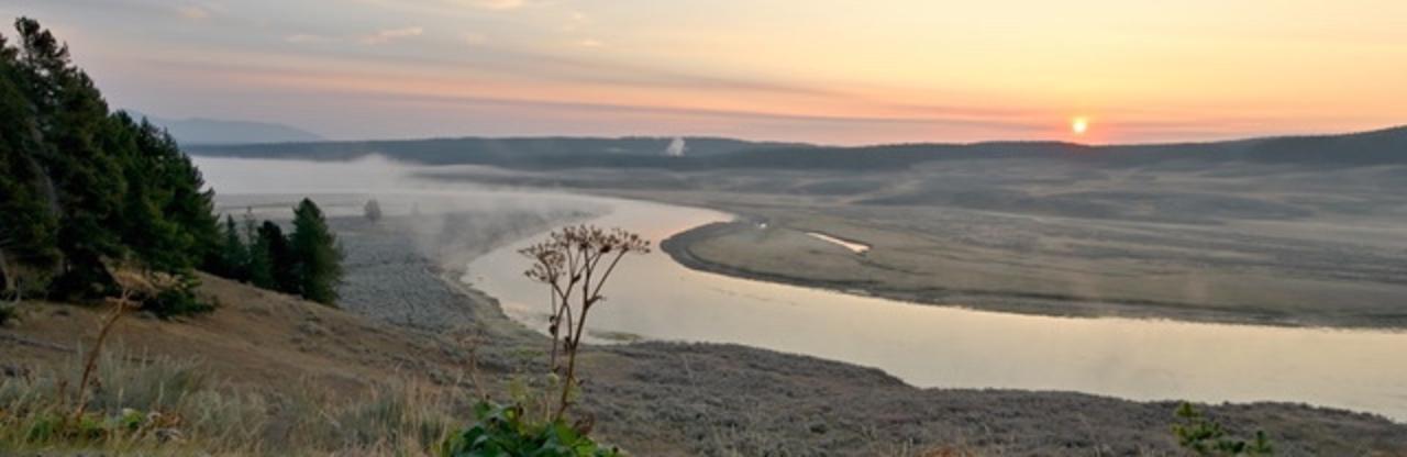 The desiccated skeleton of a cow parsnip overlooks a late autumn sunrise above an S-curve in the Yellowstone River. The lingering funk of smoke from regional late season wildfires tints the early morning light. 