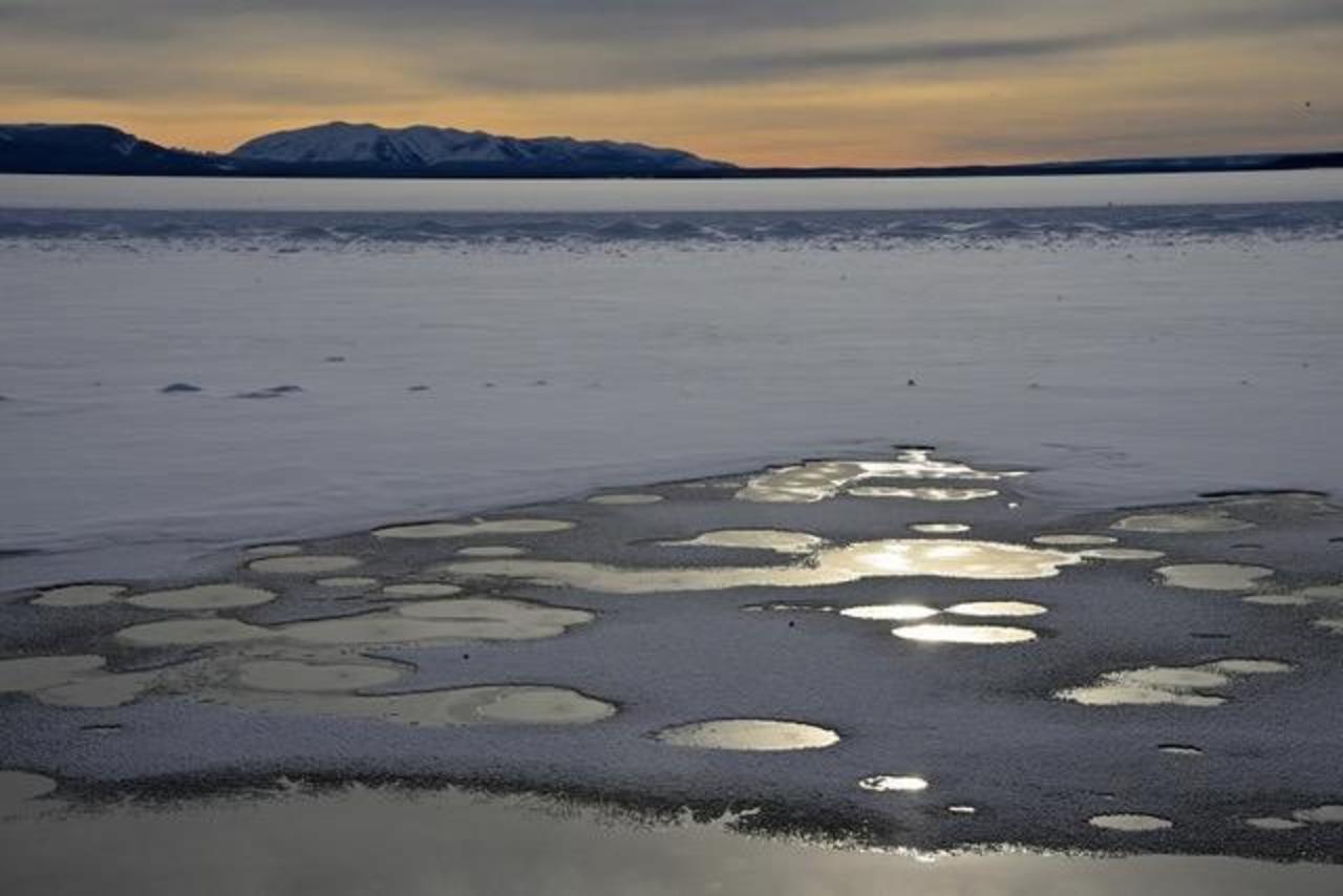 Even after the lake has frozen many hot springs on the floor of the lake keep circular windows open in the overlying ice cover. In the middle distance a row of ice-bound "fossil frazil" cones mark the previous edge of open water.