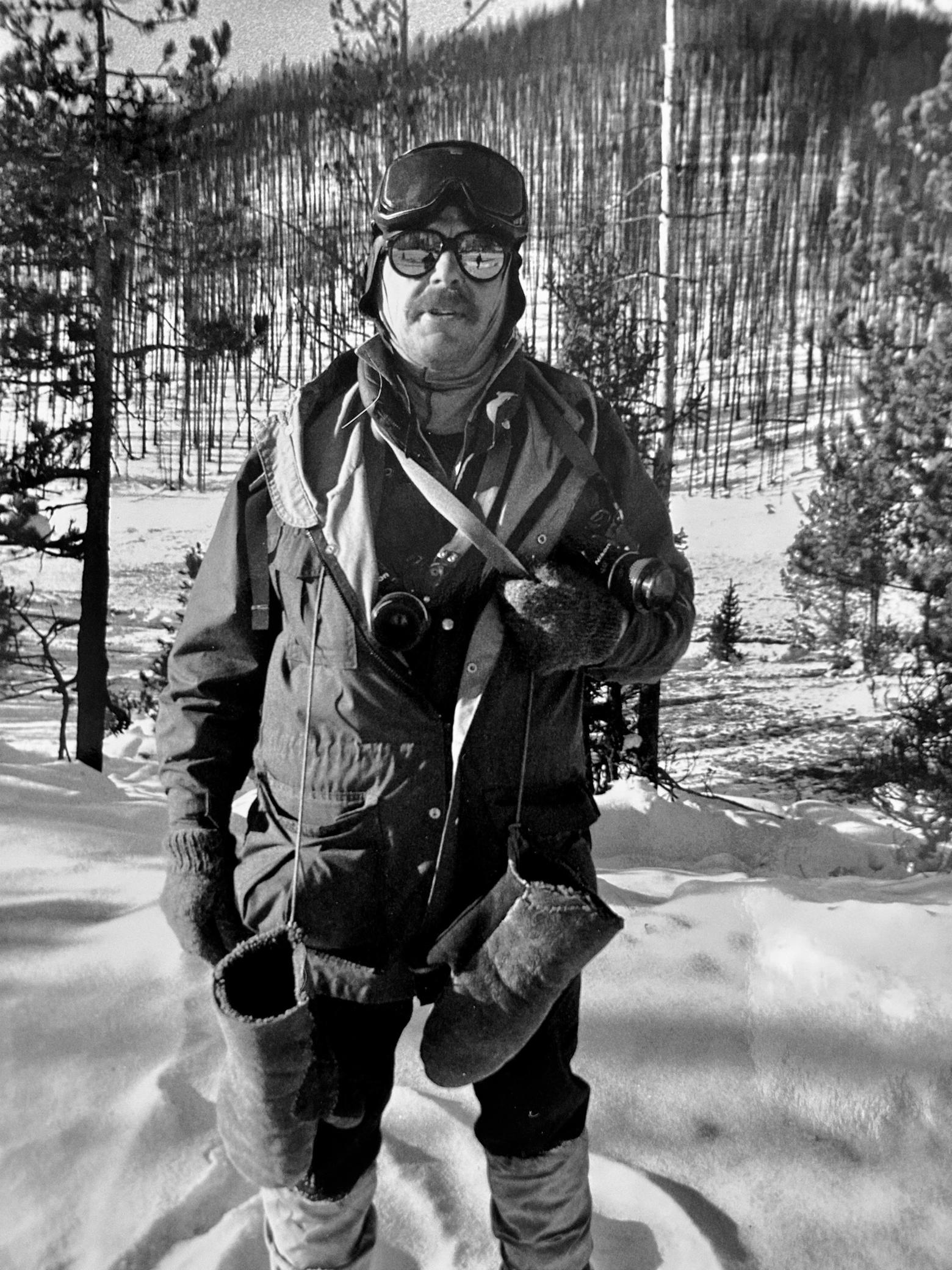 Not your average snowmobile attire yet fashionable for the time: winterkeeper Steve Fuller looks more like a WWII bomber pilot or Arctic explorer. Never without a camera, here he makes a pit stop at Roaring Mountain on his way back to Canyon from Mammoth Hot Springs via snowmobile in January 1989. The lodgepole pine forest behind him had burned only a few months earlier during the historic 1988 Yellowstone fires. The ambient temperature on that day was minus 25 degrees F. Photo by Todd Wilkinson
