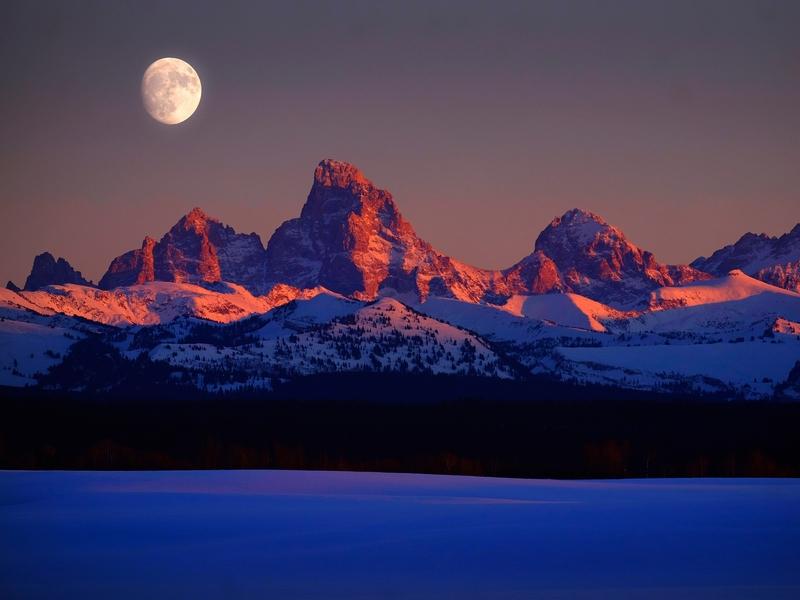 Sunset, amid moonrise, brings alpenglow to the west side of the Tetons above Teton Valley, Idaho