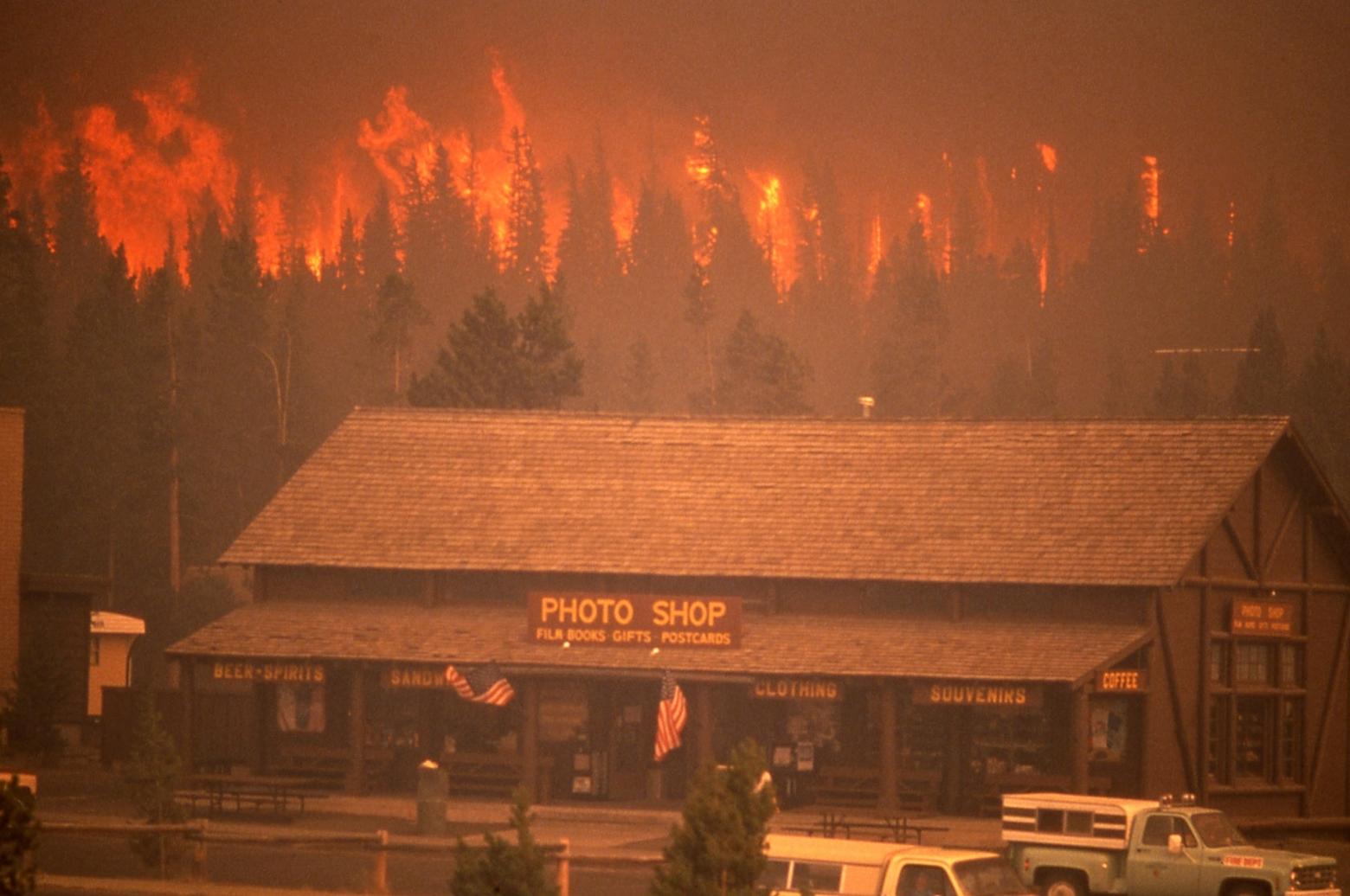 A cautionary tale: In the summer of 1988, winds gusting upwards of 80 mph fanned wildfires that burned nearly 800,000 acres in Yellowstone National Park. Here, a crowning North Fork Fire approaches the Old Faithful Inn complex and its Photo Shop. Photo by Jeff Henry/NPS