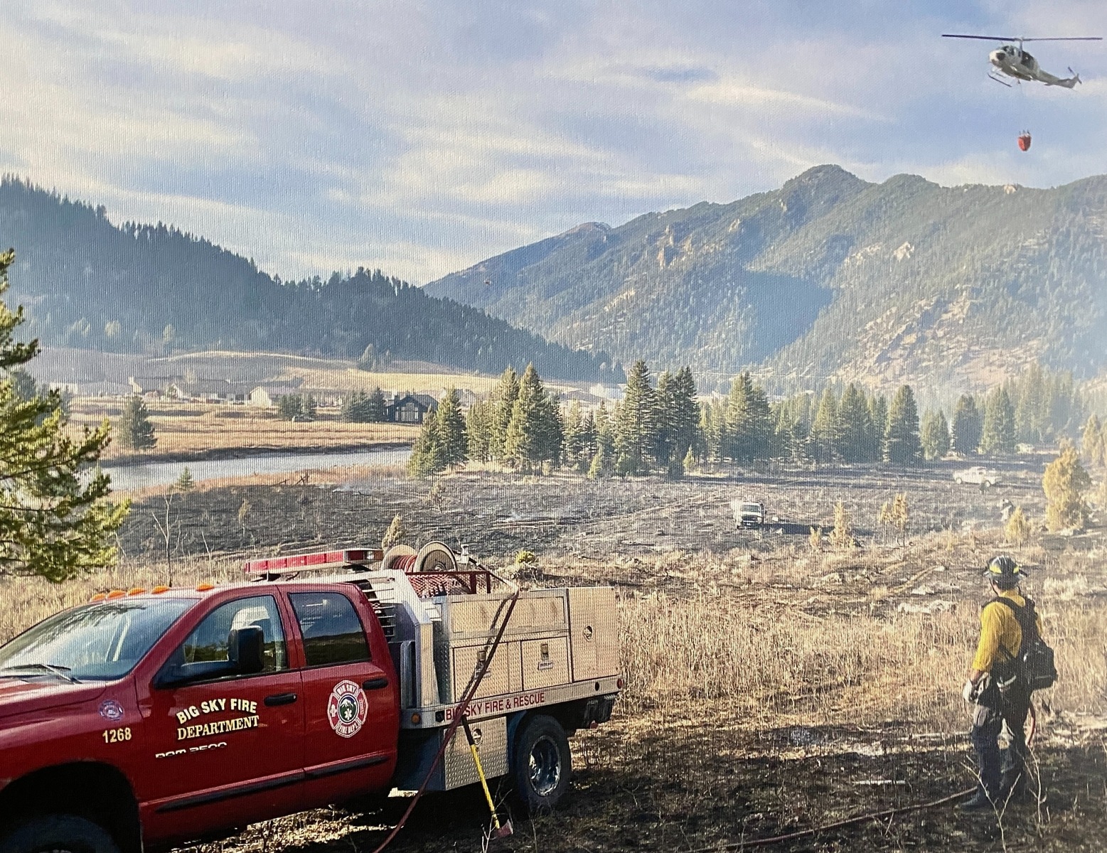 This photo of the Porcupine Fire in 2021 hangs in the halls of the Big Sky Fire Department. Helicopters pulled water from the Gallatin River beyond the burn zone. Photo courtesy BSFD