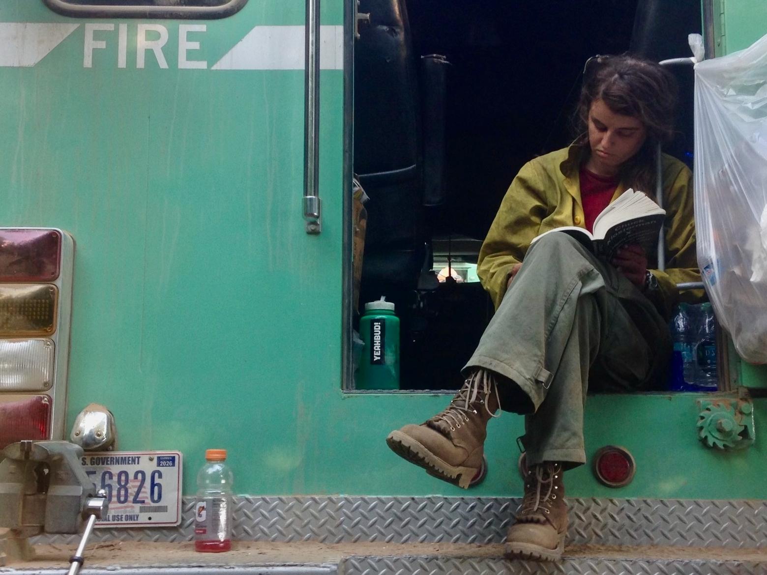 Journalist and former wildland firefighter Amanda Monthei waits out the wind with a book during a fire assignment in Oregon, 2018. Photo courtesy Amanda Monthei 