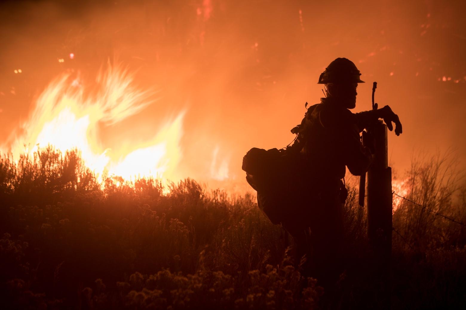 A wildland firefighter leans on his drip torch on a fence post as he takes a breather during Wyoming's Roosevelt Fire in 2018. Photo by Kari Greer